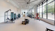 Located at 2509 N. Davidson St in Charlotte's NoDa neighborhood, this modern fitness center offers a comprehensive, single-floor workout facility designed with both functionality and aesthetics in mind. The space is defined by soaring ceilings, crisp white walls, and an abundance of natural light streaming through floor-to-ceiling windows that frame outdoor views, creating an open and energizing atmosphere throughout.

The main workout floor is generously proportioned, accommodating a wide range of cardio equipment including stair climbers, upright bikes, and elliptical machines, as well as functional training tools such as a large tire for strength conditioning. A dedicated free weights area features a full rack of dumbbells, adjustable benches, and wall-mounted mirrors with integrated LED accent lighting and flat-screen TVs for an enhanced training experience.

A separate studio space with warm hardwood flooring and full-length mirrors is equipped with cycling bikes and an interactive fitness display, ideal for group or individual spin sessions. High ceilings in this room add to the sense of openness.

The facility also includes a dual-level stainless steel water fountain with a bottle-filling station, built-in shelving, and a beverage refrigerator for member convenience. Track lighting and large ceiling fans ensure comfort across all zones, making this a well-appointed, professional-grade fitness destination.