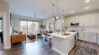 This single-floor, 2-bedroom, 2-bathroom residence in Greenwood, Indiana offers a thoughtfully designed open-concept layout that maximizes its comfortable footprint. The combined kitchen and living area serves as the heart of the home, where a sleek kitchen impresses with white shaker cabinetry extending to the ceiling, a classic subway tile backsplash, quartz countertops, stainless steel appliances, and a large center island with pendant lighting overhead. The living room flows seamlessly from the kitchen and is filled with natural light through expansive sliding glass doors that open to a private balcony with outdoor views.

The primary bedroom is a generously sized retreat with plush carpet flooring, ceiling fan, and multiple windows offering natural light. It connects directly to a well-appointed en-suite bathroom featuring a dual-sink vanity with quartz countertops, wood-look flooring, a large framed mirror, and a tiled tub-shower surround. The second bedroom is equally comfortable with carpeted floors, a ceiling fan, and outdoor-facing windows. Two dedicated closets provide ample storage. A conveniently located in-unit laundry room houses a full-size washer and dryer. Wood-look flooring throughout the main living areas ties the space together with a cohesive, modern aesthetic.