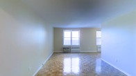 Located at 44-30 Douglaston Parkway in the charming Douglaston neighborhood of Queens, New York, this single-floor unit offers a well-proportioned and inviting living space. The interior is defined by beautifully polished parquet wood flooring laid in a classic geometric pattern, adding warmth and timeless character throughout. The main living area is generously sized, with smooth, light-toned walls that contribute to a clean and airy atmosphere. Multiple windows allow natural light to filter in, brightening the space and creating a welcoming ambiance. Radiator heating units are positioned beneath the windows, indicative of a well-established building infrastructure designed for year-round comfort. The open layout of the living area provides flexible arrangement options, making it adaptable to a variety of needs. The neutral color palette of the walls pairs seamlessly with the warm tones of the flooring, offering a versatile backdrop for any interior style. Overall, this unit combines classic architectural details with a practical layout, situated in the sought-after and residential Douglaston community of northeastern Queens.