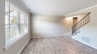 Located at 338 S Chesire Ct in Virginia Beach, VA, this two-story, 2-bedroom, 2-bathroom home offers a thoughtfully laid-out floor plan spread across two levels. The main floor features a bright and open living room adorned with crown molding, neutral-toned walls, and light luxury vinyl plank flooring that flows throughout the common areas. Natural light streams in through windows dressed with classic blinds. The combined kitchen and dining area is well-appointed with crisp white cabinetry, marble-look countertops, a stainless sink, and black appliances including a range, over-the-range microwave, and dishwasher. A dedicated laundry area and ample closet storage add practical convenience. An elegant wrought-iron staircase railing leads to the upper level, where both bedrooms are carpeted and each features a ceiling fan with light kit. The spacious primary bedroom includes multiple closets, providing generous storage. Both bathrooms are finished with white vanities, wood-look LVP flooring, and clean fixtures; one features a full tub/shower combo, while the other offers a compact design tucked beneath a sloped roofline. The home's neutral color palette and updated finishes throughout create a clean, move-in-ready atmosphere.