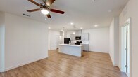 This thoughtfully designed single-story home in Baton Rouge, Louisiana offers a clean, modern aesthetic throughout its three bedrooms and two bathrooms. The open-concept living and kitchen area serves as the heart of the home, anchored by a striking center island topped with marble-look quartz countertops and illuminated by elegant pendant lighting. The kitchen is well-equipped with gray shaker-style cabinetry, a white subway tile backsplash, matching quartz counters along the perimeter, and a full suite of black appliances. Warm-toned luxury vinyl plank flooring runs throughout the main living areas, complemented by ceiling fans that add both style and comfort. The bedrooms offer plush carpeting underfoot, ceiling fans, and natural light from well-placed windows with blinds. The spacious primary bedroom connects to a private bathroom featuring a gray double vanity with quartz countertops and wood-look flooring. A dedicated walk-in closet with built-in shelving and hanging rods provides generous storage. The second bathroom mirrors the same refined finishes found throughout the home. Crisp white walls and recessed lighting create a bright, welcoming ambiance across every room, making this home a polished and functional living space.
