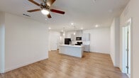 This thoughtfully designed single-story home in Baton Rouge, Louisiana offers a clean, modern aesthetic throughout its three bedrooms and two bathrooms. The open-concept living and kitchen area serves as the heart of the home, anchored by a striking center island topped with marble-look quartz countertops and illuminated by elegant pendant lighting. The kitchen is well-equipped with gray shaker-style cabinetry, a white subway tile backsplash, matching quartz counters along the perimeter, and a full suite of black appliances. Warm-toned luxury vinyl plank flooring runs throughout the main living areas, complemented by ceiling fans that add both style and comfort. The bedrooms offer plush carpeting underfoot, ceiling fans, and natural light from well-placed windows with blinds. The spacious primary bedroom connects to a private bathroom featuring a gray double vanity with quartz countertops and wood-look flooring. A dedicated walk-in closet with built-in shelving and hanging rods provides generous storage. The second bathroom mirrors the same refined finishes found throughout the home. Crisp white walls and recessed lighting create a bright, welcoming ambiance across every room, making this home a polished and functional living space.
