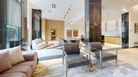 Located at 202 Burnhamthorpe Rd E in Mississauga, Ontario, this generously proportioned amenity space offers a refined and contemporary environment spread across a single floor. The space is divided into two distinct yet complementary areas, unified by high-end finishes and thoughtful design.

The main lounge and social area showcases light wood herringbone flooring, soaring ceilings with recessed coffers, and dramatic floor-to-ceiling windows that flood the space with natural light. Striking black marble columns and accent panels provide bold contrast against crisp white walls. A central round dining table with a fluted gold base and plush velvet seating anchors the room, while curated abstract artwork and sculptural gold pendant lighting add artistic flair. Additional seating areas with soft upholstered chairs create intimate gathering zones, complemented by a dedicated dining table for larger groups.

The second area serves as a games and entertainment room, featuring a full-size pool table set atop vibrant patterned carpet tiles. Warm wood-panelled walls with geometric green accent detailing and integrated linear lighting give this room a sleek, playful character. Glass-panelled doors connect the zones, maintaining visual openness while defining each space's distinct purpose. Together, these areas deliver a polished, resort-calibre amenity experience.