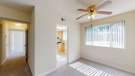 This single-floor unit is designed with a straightforward, functional layout that maximizes the use of its available space. The living area is generously proportioned, featuring neutral-toned carpet flooring and cream-painted walls that create a bright, open atmosphere. A ceiling fan with a brass finish and integrated light fixture provides both air circulation and ambient lighting, while a large window fitted with vertical blinds allows abundant natural light and outdoor views of surrounding greenery.

Adjacent to the living area, the kitchen is equipped with warm-toned wood cabinetry, dark granite-style countertops, a stainless steel sink, a gas range, and a full-size refrigerator. Light tile flooring completes the practical yet welcoming cooking space.

The bedroom offers comfortable proportions, continuing the carpeted flooring, and includes a ceiling fan, a window with vertical blinds for natural light, and an open closet for storage.

The bathroom is clean and straightforward, featuring white-tiled walls surrounding a full bathtub and shower, a wood-framed vanity with a white countertop sink, and a window that introduces natural light. Throughout, the unit maintains a consistent, neutral aesthetic.
