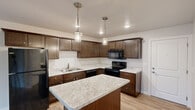 This single-floor residence offers a thoughtfully designed layout that balances functionality and comfort throughout. The kitchen serves as a central highlight, showcasing rich dark wood cabinetry, marble-patterned countertops, and a generous center island that provides additional prep and seating space. A suite of black appliances, including a refrigerator, range, and over-the-range microwave, completes the space, while two elegant pendant lights hanging above the island add a stylish touch to the room's ambiance.

The bedrooms feature plush wall-to-wall carpeting and ceiling fans with integrated lighting, contributing to a comfortable and relaxed atmosphere. Natural light filters in through well-placed windows, offering pleasant outdoor views. A spacious walk-in closet with full wire shelving systems provides generous and organized storage.

The bathrooms are finished with coordinating dark wood vanities topped with marble-style counters and light wood-look flooring. One bathroom includes a tub and shower combination with a built-in shelf niche, while another offers a standalone walk-in shower with clean white surroundings.

A dedicated laundry area houses a stacked washer and dryer unit, adding a practical convenience to daily living. Throughout the residence, neutral tones, consistent finishes, and an open floor plan create a cohesive and welcoming environment.