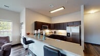 This single-floor residence is designed with a contemporary aesthetic, highlighted by dark espresso cabinetry, wood-look flooring, and a neutral color palette throughout. The kitchen serves as a central feature, offering an L-shaped layout with an extended breakfast bar accommodating bar-stool seating. Dark lower and upper cabinetry contrasts cleanly against light quartz-style countertops, while stainless steel appliances—including a refrigerator with ice maker, electric range, built-in microwave, and dishwasher—complete the well-equipped space. Under-cabinet lighting and a subtle tile backsplash add refined detail.

The dining area is positioned near large windows that frame outdoor views and draw in abundant natural light. The living area continues this bright, open character, with tall windows overlooking a green exterior landscape. Two bedrooms provide comfortable retreats, each featuring wood-look flooring and window access to natural light. Both bathrooms maintain the dark cabinetry theme, with one featuring a walk-in shower and the other a tub-shower combination with a curtain. The overall ambiance is modern, clean, and cohesive.