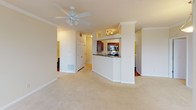 This single-floor, 2-bedroom, 2-bathroom residence offers a practical and comfortable layout designed for easy everyday living. The open living area features plush wall-to-wall carpeting, crown molding, a ceiling fan, and multiple windows fitted with blinds that allow for ample natural light while maintaining privacy. A pass-through kitchen overlooks the living space and is equipped with rich, warm-toned wood cabinetry, dark granite-style countertops, stainless steel appliances including a range, over-the-range microwave, and dishwasher, as well as hardwood-style flooring for easy maintenance. Both bedrooms are generously sized, carpeted, and feature windows that bring in natural light. The primary bathroom includes a wide vanity with dual mirrors, wood cabinetry, and hardwood-style flooring, with a separate shower and tub area. The second bathroom offers a clean, full tub-shower combo with chrome fixtures. Throughout the unit, neutral warm beige tones create a cohesive and inviting atmosphere, while consistent finishes and thoughtful design details — including crown molding in the main living area and a ceiling fan in the primary bedroom — add a polished touch to this well-appointed home.