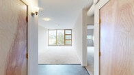 Located at 131 E Green St in downtown Ithaca, NY, this two-bedroom, two-bathroom residence offers a thoughtfully organized single-floor layout. The space is designed with clean lines and a neutral palette throughout, creating a bright and functional living environment.

The U-shaped kitchen features dark countertops that contrast sharply with white cabinetry, a stainless steel sink, and tile flooring, providing ample storage and prep space. A hallway connects the main living areas, leading to the generously sized bedrooms, both finished with plush wall-to-wall carpeting. The primary bedroom is notably spacious and is highlighted by large wood-framed windows that frame scenic outdoor views of the surrounding Ithaca landscape, filling the room with natural light. It also includes a double closet with warm-toned wood doors. The second bedroom similarly features carpeting and additional window views.

Both bathrooms are finished with dark slate-style tile flooring and include modern vanities with dark cabinetry, white countertops, and large mirrors. One bathroom features a full tub-shower combination equipped with safety grab bars. The overall aesthetic is contemporary and understated, offering a clean, move-in-ready environment in a prime Ithaca location.