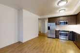Located at 1525 SW 11th Ave in Portland, Oregon, this two-bedroom, two-bathroom residence offers a thoughtfully designed single-level layout with modern finishes throughout. The open-concept living and kitchen area is anchored by warm hardwood-style flooring, crisp white walls, and a seamlessly integrated kitchen featuring rich dark-walnut cabinetry, a herringbone tile backsplash, stainless steel appliances including a French door refrigerator, electric range, microwave, and dishwasher, plus a deep undermount sink. A sliding glass door connects the living area to a private outdoor balcony with slatted wood privacy screening. Both bedrooms are carpeted and generously proportioned, with the primary bedroom offering a sliding-door closet and direct access to its en-suite bathroom. Each bathroom is finished with a dark wood vanity, white quartz countertop, large mirror, and light tile flooring. The primary bath includes an additional walk-in closet visible from the vanity area. The second bedroom features a window with exterior views and its own adjacent bathroom. Two hallways connect the space efficiently, contributing to a clean and functional flow throughout this well-finished Portland residence.