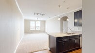 This single-floor residence offers a thoughtfully designed open-concept layout that seamlessly connects the kitchen and living area. The kitchen is a standout feature, showcasing rich dark cabinetry, granite countertops, a center island with a built-in sink, stainless steel appliances, and warm hardwood-style flooring. Elegant pendant lighting hangs above the island, complemented by track lighting overhead, while a graceful arched passageway adds a refined architectural detail. Crown molding runs throughout the main living areas, enhancing the overall sense of polish and quality.

The expansive living area flows naturally from the kitchen, featuring plush carpeting, a ceiling fan, and a window that invites natural light into the space. A glass-paneled door provides additional light and outdoor access. The bedrooms are generously sized, each finished with soft carpet, neutral warm-toned walls, and windows with blinds for privacy and light control.

The bathroom is well-equipped with a granite-topped dark vanity, a combination tub and shower, and hardwood-style flooring that ties back to the kitchen aesthetic. Throughout the residence, the consistent use of neutral tones, quality finishes, and practical design choices create a cohesive, comfortable, and move-in-ready living environment.