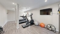 Located at 1001 N Donahue Dr in Auburn, Alabama, this single-floor fitness center offers a well-equipped exercise space designed to support a variety of workout routines. The room features light wood-look luxury vinyl flooring, neutral gray walls, and recessed lighting, creating a clean and inviting atmosphere throughout.

The space is outfitted with multiple cardio machines, including two Star Trac treadmills and an elliptical trainer, positioned to take advantage of the natural light streaming in through several windows fitted with horizontal blinds. A wall-mounted flat-screen TV adds a convenient entertainment option for cardio sessions.

Strength training is well supported by a Hoist functional trainer cable machine, along with a tiered dumbbell rack stocked with a range of free weights and an aerobic step platform. Stability balls in multiple sizes are available for core and balance work, and an open stretching area with exercise mats provides space for floor-based training and cooldown routines.

Structural columns are integrated into the layout, subtly defining different workout zones without interrupting the flow of the space. Safety features include a fire extinguisher and clearly posted informational signage near the entrance. The abundance of windows ensures the room remains bright and connected to the outdoors, contributing to an energizing and functional workout environment.