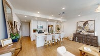 This two-story home is designed with a clean, modern aesthetic defined by neutral tones, light wood-look flooring, and an abundance of recessed lighting throughout. The open-concept main living area seamlessly connects the kitchen and living space, creating an expansive, airy atmosphere well-suited for both daily living and entertaining. The kitchen is outfitted with crisp white cabinetry, light countertops, and stainless steel appliances, including a range, microwave, and refrigerator. A generously sized island with bar seating serves as a central gathering point. The welcoming entryway features a sidelight window beside the front door, allowing natural light to filter in, and offers comfortable space for seating or a console. Bedrooms are carpeted and well-lit by large windows with blinds, each featuring ceiling fans. A spacious walk-in closet provides ample wire shelving for organized storage. The bathroom includes a white vanity with light countertops and a tub-shower combination. The attached garage features a concrete floor and drywall-finished walls with an automatic door opener, offering practical everyday convenience throughout this thoughtfully laid-out home.