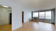 Located at 133 Park, this single-floor space offers a clean, minimalist layout designed for comfortable, functional living. The main living area is characterized by smooth light-toned hardwood flooring that extends throughout, complementing the crisp white walls and ceiling to create a bright, airy atmosphere. A large sliding glass door floods the space with natural light and provides direct access to a private balcony, where expansive outdoor views of the surrounding landscape can be enjoyed. The wall-mounted air conditioning unit ensures year-round climate comfort. A doorway connects the living area to the adjoining rooms, hinting at a thoughtful layout that maximizes the use of the available space. The overall ambiance is open, clean, and move-in ready, with a neutral palette that offers a versatile canvas for a variety of interior styles. The combination of natural light, outdoor access, and well-maintained finishes makes this a practical and inviting space at 133 Park.