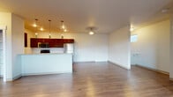 Located at 16511 East Sprague Avenue in Spokane Valley, Washington, Unit F8 is a thoughtfully designed residential unit accessed by a carpeted staircase with a handrail and wall sconce lighting. The main living level features an open-concept layout with durable wood-look flooring that flows throughout the common areas. The kitchen is equipped with rich dark wood cabinetry, stainless steel appliances including a range, microwave, and refrigerator, and a peninsula with pendant lighting overhead that separates the kitchen from the spacious living area. A built-in shelving pantry and in-unit laundry connections are accessible just off the kitchen. The bedrooms are carpeted and offer generous space, with one bedroom featuring a closet with built-in shelving and direct access to a hallway. Each bathroom is outfitted with a soaking tub and shower combination, with one bathroom showcasing a dark wood vanity with a stone-top countertop and wood-look flooring, while a second bathroom features tile flooring and a similar tub-shower setup. Neutral tones throughout the unit create a clean, move-in-ready atmosphere, and windows provide natural light and exterior views of the surrounding Spokane Valley neighborhood.