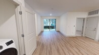 Located at 700 Henley St in downtown Knoxville, Tennessee, this thoughtfully designed single-floor unit offers a clean, modern aesthetic throughout. The open-concept living area features light wood-tone flooring and bright white walls, creating an airy and welcoming atmosphere. Sliding glass doors provide direct access to an outdoor patio, allowing natural light to fill the main living space and offering views of the surrounding community.

The kitchen is a standout feature, showcasing bold navy-blue cabinetry with gold-toned hardware, a white tile backsplash, light countertops, and a full suite of stainless steel appliances including a refrigerator, range, microwave, and dishwasher. The kitchen flows seamlessly into the living area, making it ideal for everyday functionality.

The bedroom is generously sized with plush carpet flooring and ample wall space, complemented by a spacious walk-in closet with wire shelving. The unit includes two bathrooms finished with light marble-look tile flooring, white cabinetry with gold hardware, and expansive vanity mirrors. The primary bathroom features a glass-enclosed walk-in shower with elegantly tiled walls. A dedicated laundry area with a full-size front-loading washer and dryer adds further convenience to this well-appointed unit.
