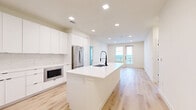 This modern 2-bedroom, 1-bathroom home in Round Rock, TX offers a thoughtfully designed open-concept layout with clean lines and a bright, contemporary aesthetic. Light wood-tone flooring runs throughout, creating a warm and cohesive feel across every room.

The kitchen is a standout feature, showcasing floor-to-ceiling white cabinetry, a marble-look tile backsplash, and a large central island with a white quartz countertop and matte black undermount sink. Stainless steel appliances — including a French door refrigerator, electric range with wall-mounted hood, built-in microwave, and dishwasher — complete this well-appointed space. Recessed lighting keeps the area bright and functional.

The open living area extends naturally from the kitchen, bathed in natural light from a double glass door that opens to an outdoor balcony, offering views of the surrounding landscape. Both bedrooms are generously sized, with large windows that invite natural light and ceiling fans for comfort. The primary bedroom includes access to a dedicated closet.

The bathroom is elegantly finished with a double-sink vanity topped with white quartz, illuminated mirrors with matte black hardware, a glass-enclosed tiled shower, and continued wood-look flooring. Two closets provide ample storage throughout the home. Clean, neutral tones and modern finishes give this space a fresh, move-in-ready appeal.