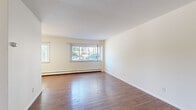 Located at 242 W Franklin Ave in Minneapolis, MN, this two-bedroom, one-bathroom unit offers a practical and well-organized floor plan across a single level. The living room is a bright, open space featuring rich hardwood-style flooring and large windows that invite generous natural light and views of the surrounding neighborhood. Baseboard heating runs along the perimeter, ensuring consistent warmth throughout.

The kitchen is efficiently designed with warm wood cabinetry, a double-basin sink, a white electric range, and a full-size refrigerator — providing ample storage and functionality for everyday cooking. Hardwood-style flooring continues here, maintaining a cohesive look.

Both bedrooms are carpeted for comfort and feature vertical blinds over sizable windows that bring in natural light. The primary bedroom offers notably generous dimensions, while the second bedroom includes a built-in closet with sliding doors. Baseboard heaters are present in both rooms.

The bathroom is finished with classic white tile wainscoting, mosaic tile flooring, a vanity with cabinet storage, and a bathtub — offering a clean, functional layout. A connecting hallway ties all rooms together efficiently, completing this straightforward and comfortable floor plan.
