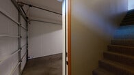Located in Spokane Valley, WA, this two-story, one-bedroom, one-bathroom unit offers a well-organized layout across two levels. The ground floor houses a private, enclosed garage with a concrete floor, automatic door opener, and direct interior access via a carpeted staircase leading up to the main living area.

The upper level encompasses the majority of the living space. The open-concept kitchen features warm-toned wood cabinetry, a tile backsplash, stainless steel appliances including a refrigerator, microwave, and electric range, and a large peninsula with a flat countertop that separates the kitchen from the carpeted living area. Pendant lighting adds a decorative touch overhead. The living room is generously sized, bathed in natural light through a large window and glass door that opens to an exterior view.

The bedroom is a comfortable size, finished with plush carpet and flanked by two wood doors — one leading to a walk-in closet equipped with wire shelving and a water heater. The full bathroom features tile flooring, a tub/shower combo with built-in shelving, a wood-cabinet vanity, and a large mirror. A dedicated laundry area includes a full-size washer and dryer with overhead shelving. A hallway ties the rooms together efficiently, completing this functional and well-appointed layout.