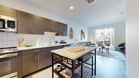 This single-floor residence at 40 Bennett Road in Englewood, New Jersey, showcases a thoughtfully designed open-concept layout with contemporary finishes throughout. The kitchen is a standout feature, equipped with dark wood-grain cabinetry, white quartz countertops, a classic subway tile backsplash, and a full suite of stainless steel appliances, including a refrigerator, range, and microwave. A freestanding kitchen island with a stone top provides additional prep and dining space, while light hardwood flooring flows seamlessly into the adjacent dining and living areas.

The living room is bright and welcoming, benefiting from natural light that pours in through large sliding glass doors leading to a private outdoor patio. The space offers comfortable room for seating and entertainment, with clean white walls and a relaxed, modern ambiance. A dedicated dining nook nearby accommodates casual meals with ease.

The bedroom is a calm retreat, featuring soft neutral wall tones, a large window that enhances natural light, and ample room for furnishings. Light hardwood flooring continues throughout, maintaining visual cohesion across the home. The overall design balances modern aesthetics with functional, everyday comfort, making this Englewood residence a well-appointed and inviting living space.