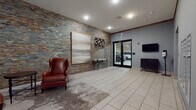 320 Valley presents a well-appointed lobby and common area space designed with both aesthetics and functionality in mind. The entrance lobby immediately establishes a polished, modern identity, anchored by a dramatic stacked stone accent wall in earthy tones of gray, rust, and gold. The building's bold "320 Valley" signage is mounted directly onto this feature wall, creating a strong first impression. Light-toned large-format tile flooring transitions seamlessly into a textured area rug, defining a comfortable lounge seating area furnished with rich cognac leather wingback chairs and a round side table, offering residents a welcoming space to gather.

Recessed lighting throughout the lobby ensures consistent illumination, while a wall-mounted flat-screen television and a sleek cabinet add modern convenience near the double-glass doors leading to the attached parking structure. The lobby also includes a hand sanitizer station and intercom system, reflecting thoughtful attention to resident needs.

Direct access to a generously sized covered parking garage is available through the glass double doors, where concrete structural columns and bright overhead lighting accommodate numerous vehicles with ease. Adjacent to the garage entrance, residents will find a stainless steel elevator and a built-in bank of individual mailboxes, rounding out a comprehensive and efficiently organized ground-floor common area experience.