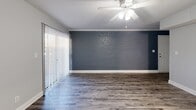 Located in Charlotte's 28205 zip code, this single-story, three-bedroom, two-bathroom home offers a practical and comfortable layout throughout its well-organized floor plan. The living room is an immediate standout, featuring a painted exposed brick accent wall, wood-look hardwood-style flooring, a ceiling fan, and sliding glass doors dressed with vertical blinds that invite natural light and outdoor access. The kitchen is efficiently designed with white cabinetry, white countertops, a stainless steel sink, and white appliances including a range, built-in microwave, dishwasher, and refrigerator. A stacked washer and dryer unit is conveniently integrated into the kitchen area. The bedrooms offer soft carpeted flooring and neutral gray walls. The primary bedroom is a comfortable size with a wide window for natural light and a ceiling fan overhead. The additional bedrooms are versatile, with one featuring vertical blinds and wood-look flooring, and another with carpet and ample wall space. Both bathrooms are finished in a clean, all-white palette with tub-shower combinations, white vanities, and wood-look flooring. This home presents a cohesive, move-in-ready aesthetic with consistent neutral tones throughout.