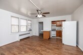 Located at 4200 Grand Ave in Des Moines, Iowa, this efficient single-floor unit offers a well-organized layout that makes the most of its compact footprint. The open living area is bright and welcoming, featuring warm hardwood flooring, white walls, and a ceiling fan with light fixture overhead. Natural light filters in through multiple windows fitted with blinds, while a baseboard radiator and window A/C unit provide year-round climate comfort. The kitchen is thoughtfully arranged with warm oak cabinetry, white tile backsplash, white tile flooring, a gas range, and a full-size refrigerator. A peninsula counter with a white laminate top extends into the living area, creating a natural divide and added prep space. The bathroom retains classic mid-century character, showcasing peach ceramic wall tiles accented by a black tile border, a tiled tub surround, marble-look flooring, a window for natural ventilation, a vanity with sink, and a radiator. A hallway connects the main living spaces to a closet and bathroom, contributing to the unit's organized flow. Overall, the space offers a clean, functional, and straightforward living environment with a warm, timeless aesthetic.
