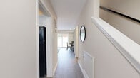 This two-story home in Richmond, Virginia offers a well-organized layout spread across two floors, thoughtfully designed to maximize comfort and functionality. The main level features a bright, welcoming living room with wood-look flooring, neutral walls, and a sliding glass door that fills the space with natural light. A connected hallway leads to the kitchen, which is equipped with a full-size refrigerator, and flows seamlessly toward the dining area. A round decorative mirror accents the hallway, adding a stylish touch to the clean, minimal aesthetic. The main floor also includes a bathroom featuring classic white subway tile, a tub-shower combination, and wood-look flooring for a warm contrast. Upstairs, the spacious primary bedroom offers plush carpeting, dual windows that invite generous natural light, and a comfortable, restful atmosphere. The second bedroom, also carpeted, provides a cozy and versatile space. A dedicated hallway and closet on the upper level add to the home's practical storage solutions. Throughout both floors, the design maintains a cohesive palette of soft neutrals accented by crisp white trim, creating a clean and inviting ambiance. The overall layout is efficient and well-suited for everyday living.