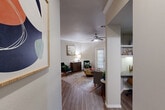Located in Houston, TX, this single-story 2-bedroom, 2-bathroom residence offers a thoughtfully designed layout with consistent wood-look flooring and a neutral color palette throughout. The living room is bright and welcoming, featuring crown molding, a ceiling fan, and a large window that draws in natural light. Track lighting and open wall space add versatility to the adjacent dining area. The kitchen is equipped with white shaker cabinetry, granite countertops, a subway tile backsplash, and stainless steel appliances, including a refrigerator, range, and microwave. A breakfast bar opening connects the kitchen to the main living area, while a hallway with built-in open shelving provides convenient storage. The primary bedroom is generously sized with a ceiling fan, a large window overlooking greenery, and direct access to an en-suite bathroom featuring a walk-in shower and granite vanity. The second bedroom is well-sized with a ceiling fan and ample natural light. A second full bathroom includes a tub-shower combination with white tile surround and white cabinetry. Crown molding in key areas and clean, modern finishes throughout contribute to a cohesive and comfortable ambiance across this efficiently designed home.