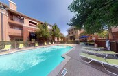 Located at 2101 N Haskell Ave in the heart of Dallas, Texas, this outdoor amenity space offers a welcoming retreat from the urban environment. The centerpiece of the space is a generously sized swimming pool with clear, turquoise water, providing a refreshing escape during warm Texas days. The pool area is finished with a textured concrete deck that surrounds the water on multiple sides, offering ample room for relaxation and leisure.

The sun deck is well-appointed with green lounge chairs and chaise lounges, inviting residents and guests to unwind in the open air. A shaded seating area with a blue market umbrella provides a comfortable alternative for those seeking relief from direct sunlight. The pool area is enclosed by a wrought iron fence, providing both security and a clear boundary for the amenity space.

Mature trees are interspersed throughout the area, offering natural shade and a touch of greenery that softens the surrounding brick architecture. The multi-story brick residential buildings frame the pool area, creating a courtyard-like atmosphere. The space benefits from abundant natural light under open skies, making it an ideal outdoor gathering and recreation area within this Dallas community.