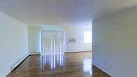 Located at 130 Aberdeen Red in Matawan, New Jersey, this single-floor space offers a straightforward and functional layout with a bright, open feel throughout. The main living area is highlighted by polished hardwood floors that reflect natural light, contributing to an airy and well-lit atmosphere. Large vertical blinds cover a full sliding glass door, allowing for flexible light control while also providing access to the outdoors. A wall-mounted air conditioning unit ensures year-round comfort, complemented by baseboard heating along the perimeter walls. The walls are finished in a clean, neutral white, creating a versatile backdrop that suits a variety of interior styles. An additional window in the adjoining area further enhances the natural brightness of the space. The open-plan design promotes a seamless flow between living areas, making the space feel expansive and welcoming. Overall, the unit presents a clean, move-in ready environment with practical amenities and classic finishes that appeal to a wide range of occupants.