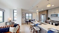 Located at 360 Huguenot Street in New Rochelle, NY, this two-bedroom, two-bathroom residence offers a thoughtfully designed single-floor layout with modern finishes and abundant natural light. Light hardwood flooring flows throughout the open-concept living areas, creating a cohesive and airy feel.

The kitchen is a standout feature, equipped with dual-tone cabinetry — combining high-gloss upper cabinets with wood-grain lower cabinets — paired with white quartz countertops and a generous island with bar seating. Pendant lighting and stainless steel appliances complete the space. The adjoining dining area accommodates a full table and benefits from city views through large windows.

The living room features floor-to-ceiling windows on multiple walls, filling the space with natural light and offering elevated views of the New Rochelle skyline. Both bedrooms are well-proportioned, with large windows framing city and neighborhood views. The primary bedroom includes expansive glazing that maximizes the outlook.

Both bathrooms are finished with large-format tile, glass-enclosed showers, and clean white vanities with dark countertops, providing a polished, contemporary aesthetic throughout.