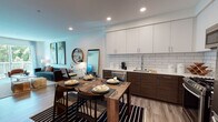 Located at 1331 N Cahuenga Blvd in the heart of Hollywood, Los Angeles, this single-floor residence offers a thoughtfully designed open-concept layout with modern finishes throughout. The kitchen is a standout feature, showcasing two-tone cabinetry with white upper cabinets and rich dark wood lower cabinets, a classic subway tile backsplash, light quartz countertops, and a full suite of stainless steel appliances including a gas range, microwave, and French door refrigerator. The kitchen flows seamlessly into the dining area, which accommodates a wooden dining table, and continues into the living room. The living space is bright and welcoming, featuring wood-look flooring, recessed lighting, and a large sliding glass door that opens to a balcony with lush greenery views, allowing abundant natural light to fill the room. The bedroom is generously proportioned, with large windows framed by sheer draping curtains that invite natural light and outdoor views. Bold, colorful artwork accents both the living room and bedroom, lending the space a vibrant, curated aesthetic. The bathroom is clean and functional, featuring a soaking tub with shower combination, wood-look tile flooring, and a dark wood vanity. Throughout the unit, the design balances contemporary style with warm, inviting tones.