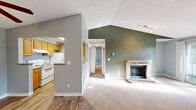 This well-appointed three-bedroom, one-bathroom residence in Seattle, WA offers a thoughtfully designed single-level layout. The living room is a standout feature, boasting vaulted ceilings with an angled accent wall painted in a rich sage green, a classic brick fireplace, and sliding glass doors that open to a private balcony with tree-lined views. Track lighting adds a modern touch to this inviting gathering space.

The galley-style kitchen is efficiently laid out with warm wood cabinetry lining both sides, laminate countertops, wood-look flooring, and white appliances including a range and refrigerator. A pass-through window connects the kitchen to the living area, enhancing the open feel. A dedicated in-unit laundry closet with a full-size washer and dryer adds everyday convenience.

The three bedrooms are finished with neutral carpet and soft gray walls, providing a calm and restful atmosphere. The primary bedroom includes dual sliding-door closets for generous storage. Additional bedrooms feature windows with natural light and baseboard heating. The bathroom offers a full tub-shower combination. A central hallway connects all rooms, creating a functional and cohesive floor plan throughout.