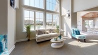Located at 100 Isabelle Isle in Dover, Delaware, this single-floor community clubhouse is designed to impress with its sophisticated yet welcoming atmosphere. The space is defined by soaring, double-height ceilings and expansive floor-to-ceiling arched windows that flood the interior with abundant natural light and frame picturesque views of the outdoor pool and surrounding community.

The main gathering area features open, generously proportioned lounge spaces furnished with elegant neutral tones and vibrant teal accents, creating an inviting and stylish ambiance. A striking reclaimed wood accent wall adds a warm, rustic contrast to the otherwise clean, contemporary aesthetic. Plush carpeting flows throughout the social areas, complementing the light-filled, airy atmosphere.

A dedicated workspace area provides seating and work surfaces, making the clubhouse versatile for a variety of uses. Adjacent to the main lounge, a fully equipped kitchen features crisp white cabinetry, granite countertops, a stone tile backsplash, stainless steel appliances, and a stunning warm wood plank ceiling — a refined contrast of textures that elevates the space. Light hardwood-style flooring and large windows maintain the bright, open feel throughout the kitchen as well.

Together, the architectural details, natural light, pool views, and thoughtful design make this clubhouse an exceptional gathering destination.