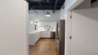 This single-floor unit blends modern design with industrial character, creating a distinctive and functional living space. The standout architectural feature is the exposed black steel ceiling structure, which soars overhead and adds dramatic visual depth throughout the unit while contributing to an open, loft-like atmosphere.

The kitchen is well-appointed and thoughtfully designed, featuring white shaker-style cabinetry with sleek chrome hardware, white quartz countertops, and a striking white subway tile backsplash accented with bold black tile inserts. Stainless steel appliances — including a French door refrigerator, range with overhead microwave, and dishwasher — complete the space. Pendant lighting and track lighting illuminate the kitchen, enhancing its clean, contemporary aesthetic.

The living and bedroom areas are bright and open, benefiting from multiple windows that bring in natural light and offer views of the surrounding neighborhood. Warm wood-look flooring flows consistently throughout, grounding the space with a natural, inviting tone that complements the industrial ceiling above. A ceiling fan in the main living area adds both function and comfort.

The bathroom continues the cohesive design language with matching white tile work featuring black accent tiles, a white vanity with undermount sink, and a glass-enclosed walk-in shower with dark tile surround. The overall ambiance of the unit is clean, modern, and well-balanced.