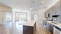 Located at 11501 W 81st St in Lenexa, Kansas, this thoughtfully designed 3-bedroom, 3-bathroom residence offers a contemporary open-concept floor plan with modern finishes throughout. The combined kitchen and living area serves as the heart of the home, featuring a large center island with a quartz-style countertop, dark espresso cabinetry, stainless steel appliances, a tile backsplash, and pendant lighting that draws the eye upward to soaring ceilings. Wood-look flooring flows throughout the main living areas, while recessed lighting and a ceiling fan add both function and style. The living room is bathed in natural light from large sliding glass doors that open to a private balcony with outdoor views. The generously sized primary bedroom includes plush carpet, high ceilings, a walk-in closet with wire shelving, and direct access to a well-appointed en-suite bathroom. A stylish barn door accents one of the additional bedrooms, which also connects to its own bathroom. Each bathroom is finished with quartz countertops, dark wood vanities, and large mirrors. The dedicated laundry room includes cabinetry and countertop space for added convenience. This residence combines modern design with practical living in a well-located Lenexa community.