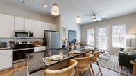 This single-floor residence offers a thoughtfully designed open-concept layout that seamlessly connects the kitchen, dining, and living areas. The kitchen is a standout feature, showcasing dark granite countertops, white shaker cabinetry, a subway tile backsplash, and a full suite of stainless steel appliances, including a French door refrigerator, electric range with over-the-range microwave, and a undermount sink. A spacious island with pendant lighting above serves as both a prep area and a casual dining space, accommodating multiple bar-height chairs. Light wood-style flooring runs throughout the main living areas, contributing to a warm and cohesive aesthetic.

The living room is bright and welcoming, benefiting from large windows and a set of French doors that invite abundant natural light and outdoor views. A ceiling fan adds to the comfort of the space. The bedroom offers a calm retreat with neutral tones, light-filtering curtains, and wood-style flooring. The en-suite bathroom features a dark granite vanity countertop, white shaker cabinetry, a large framed mirror, and clean tile flooring, providing a polished and functional space. Overall, the residence presents a modern, cohesive design with quality finishes throughout.