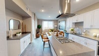 This thoughtfully designed 1-bedroom, 1-bathroom unit offers a cohesive open-concept layout that maximizes every square foot of its compact floor plan. The kitchen serves as the centerpiece of the living space, featuring a large quartz-topped island with bar seating, white shaker cabinetry, stainless steel appliances including a gas cooktop and dishwasher, and a sleek stainless steel island range hood overhead. Wood-look flooring flows seamlessly throughout, tying the kitchen, dining, and living areas together in a warm, unified aesthetic. The living room is bathed in natural light from a large picture window that frames broad city views, creating an airy, open atmosphere. The bedroom continues the bright theme with its own generously sized window overlooking the cityscape, offering a serene retreat. The bathroom is well-appointed with white cabinetry, a quartz countertop, an undermount sink, a backlit vanity mirror, and a glass-enclosed shower, all finished in a clean, contemporary style. Warm neutral tones are used consistently across the unit, contributing to a calm and inviting ambiance. Recessed lighting throughout ensures the space remains well-lit at all times of day.