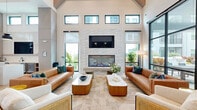 Located at 526 Vistera Blvd in Venice, Florida, this single-story community clubhouse offers a generously sized, open-concept living space designed with contemporary coastal sophistication. The space is defined by dramatically high ceilings accented with exposed wooden beams and clerestory windows that flood the interior with natural light, creating an airy and welcoming atmosphere throughout.

The main living area serves as the heart of the space, anchored by a striking floor-to-ceiling stacked stone fireplace topped with a wall-mounted television. Comfortable leather seating arrangements and textured area rugs provide an inviting lounge environment, while large black-framed glass walls and doors open to outdoor views of the surrounding community.

Light hardwood flooring runs throughout, lending warmth and continuity to the space. A reception and café-style counter area near the entrance features subway tile backsplash, pendant lighting, and a built-in banquette with a stone-topped communal table. A separate dining nook offers booth-style blue upholstered seating alongside large windows with outdoor views, ideal for casual gatherings.

A vibrant tropical mural serves as a bold focal point in one alcove, adding an artistic and energetic accent to the otherwise neutral palette. Additional rooms, including what appears to be a pet spa and a private meeting or dining room, are accessible via black-framed glass doors, rounding out this well-appointed and versatile community hub.