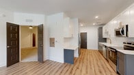 Located at 1290 Old Peachtree Rd NW in Duluth, Georgia, this single-floor residence showcases a clean, contemporary design with a cohesive color palette of whites, soft grays, and warm wood tones throughout. The kitchen is a standout feature, appointed with two-tone cabinetry — white upper cabinets with gold hardware paired with gray lower cabinets — set against a classic white subway tile backsplash. Stainless steel appliances, including a French door refrigerator, range, microwave, and dishwasher, complement the crisp white countertops. Light luxury vinyl plank flooring runs through the main living and kitchen areas, adding warmth and durability. A peninsula with additional storage creates a natural division between the kitchen and the open living space, which benefits from multiple windows that invite generous natural light and outdoor views of the surrounding greenery. The bedrooms are finished with plush wall-to-wall carpeting and ceiling fans, offering a comfortable and quiet retreat. The bathroom features a full tub-and-shower combination with white subway tile surround and brushed nickel fixtures, maintaining the residence's clean aesthetic. Recessed lighting and crisp white walls are consistent throughout, lending the entire space a bright, well-maintained, and move-in-ready atmosphere.
