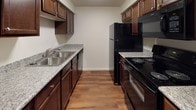 This single-floor residence at 1878 E Nine Mile Rd in Pensacola, Florida offers a well-organized layout designed for comfortable everyday living. The galley-style kitchen is efficiently appointed with rich dark wood cabinetry, granite-look countertops, a double-basin sink, and a full suite of black appliances including a refrigerator, electric range with overhead microwave, and dishwasher. Warm hardwood-style flooring runs throughout the main living areas, lending a cohesive and polished look. The living room serves as the focal point of the home, highlighted by a tile-surround fireplace with a bold floor-to-ceiling accent wall and a sliding glass door that invites natural light and outdoor views. The bedrooms feature plush carpeting, ceiling fans, ample closet space with built-in shelving, and windows that fill each room with natural light. The bathrooms are finished with dark wood vanities topped with granite-look counters, large mirrors, and updated fixtures. A second bathroom provides hardwood-style flooring and a clean, functional design. Ceiling fans are present throughout the home, contributing to year-round comfort. The overall ambiance is warm and inviting, with consistent finishes that create a cohesive aesthetic from room to room.