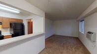 Located at 4034 Idlewild Loop in Coeur d'Alene, Idaho, this single-floor unit offers a practical and well-organized layout suited for comfortable everyday living. The kitchen is outfitted with warm honey-toned wood cabinetry, light countertops, hardwood-style flooring, a black refrigerator, dishwasher, and stove, providing ample prep and storage space. A pass-through counter opens the kitchen toward the living area, creating a connected and sociable flow between spaces. Conveniently accessible from the kitchen is a dedicated laundry room equipped with a full-size washer and dryer, along with additional shelving for storage. The spacious living room features neutral carpet and clean white walls, offering a blank canvas for personalization. The bedrooms are generously sized with plush carpeting, large windows that invite natural light and outdoor views of the surrounding neighborhood and treeline, and walk-in closets providing excellent storage. The bathroom is finished with a wood-toned vanity, light countertop, hardwood-style flooring, and a shower-tub combination. Throughout the unit, a consistent palette of neutral tones and warm wood accents creates a cohesive and inviting atmosphere.