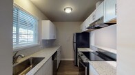 This single-floor residence offers a thoughtfully designed layout with a blend of updated finishes and functional living spaces. The galley-style kitchen is a standout feature, showcasing white shaker cabinetry, granite-look countertops, dark hardwood-style flooring, and stainless steel appliances including a range and dishwasher, complemented by an under-cabinet range hood. Natural light filters in through a window fitted with horizontal blinds, brightening the workspace on both sides of the corridor.

The open living and dining area is generously proportioned, featuring the same rich hardwood-style flooring and a textured ceiling. A sliding glass door with vertical blinds leads to an outdoor area, while an additional window ensures ample natural light. A pass-through window connects the living space to the kitchen, enhancing the open feel of the shared areas.

The bedrooms are carpeted for comfort and warmth, each featuring neutral toned walls, baseboard heating units, and windows with horizontal blinds that offer views of surrounding greenery. The bathroom is finished with a white vanity, granite-look countertops, a framed mirror, and hardwood-style flooring that extends into the hallway, which also provides access to a closet. Overall, the space presents a clean, updated aesthetic throughout.