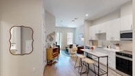 Unit 109 at 303 Lincoln St in Marlborough, Massachusetts is a thoughtfully designed one-bedroom, one-bathroom residence that maximizes its well-proportioned floor plan with modern finishes and an efficient layout. The open-concept kitchen and living area serves as the heart of the unit, featuring crisp white cabinetry, a tile backsplash, stainless steel appliances including a refrigerator, range, microwave, and dishwasher, and a marble-topped island with bar seating. Light wood-tone flooring flows throughout, enhancing the bright, airy atmosphere. The living area is bathed in natural light from large windows and a glass-panel door that opens directly to a landscaped outdoor area, offering a seamless indoor-outdoor connection. The generously sized primary bedroom accommodates a large bed with ease and includes a dedicated walk-in closet, additional windows overlooking greenery, and warm, neutral tones that create a calm retreat. The full bathroom is clean and contemporary, showcasing wood-look tile flooring, a white vanity with ample storage, and a glass-enclosed walk-in shower. Recessed lighting and a neutral color palette throughout lend the space a polished, cohesive feel suited for modern living.