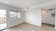 This single-story, one-bedroom, one-bathroom unit offers an efficiently organized layout across a compact but functional floor plan. The interior features a clean, modern aesthetic defined by crisp white walls, light wood-style flooring in the main living areas, and an abundance of natural light from windows fitted with horizontal blinds throughout.

The kitchen is well-appointed with dark espresso cabinetry, light countertops, and a full suite of stainless steel appliances, including an electric range, microwave, and dishwasher. A double-basin sink sits beneath a window, and recessed lighting illuminates the workspace effectively. The kitchen connects through a hallway to the remainder of the unit.

The living area is bright and open, with a structural beam detail along the ceiling and a centrally placed HVAC vent providing climate control. The space opens to a private balcony offering views of the surrounding contemporary residential community, complete with landscaping and shared amenities below.

The bedroom is carpeted for comfort and features a window overlooking the exterior, along with direct access to a dedicated walk-in closet equipped with a built-in shelf and hanging rod. The bathroom includes a full soaking tub and shower combination with white tile surround and brushed nickel fixtures.