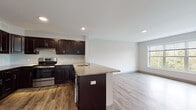 Located at 3490 Whitney Ave in Hamden, Connecticut, this single-floor residence offers a thoughtfully designed open-concept layout with contemporary finishes throughout. The kitchen serves as a central highlight, featuring rich dark espresso cabinetry, granite countertops, stainless steel appliances including a refrigerator and range, and a peninsula island with an integrated sink — ideal for both cooking and casual entertaining. Wood-look luxury vinyl flooring runs throughout the entire unit, providing a cohesive and durable foundation across all spaces. The open living area flows naturally from the kitchen, offering generous room and recessed lighting that keeps the space bright and welcoming. Bedrooms are well-proportioned, bathed in natural light through large windows that frame lush, wooded views of the surrounding landscape. One bedroom features dual closets, providing ample storage. The bathroom is cleanly appointed with a full tub-shower combination, a dark-cabinetry vanity with a light countertop, and matching flooring that ties into the rest of the unit. Neutral gray walls throughout create a clean, versatile backdrop. The overall ambiance is modern, fresh, and move-in ready, offering a serene retreat with natural scenery just outside every window.