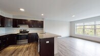 Located at 3490 Whitney Ave in Hamden, Connecticut, this single-floor residence offers a thoughtfully designed open-concept layout with contemporary finishes throughout. The kitchen serves as a central highlight, featuring rich dark espresso cabinetry, granite countertops, stainless steel appliances including a refrigerator and range, and a peninsula island with an integrated sink — ideal for both cooking and casual entertaining. Wood-look luxury vinyl flooring runs throughout the entire unit, providing a cohesive and durable foundation across all spaces. The open living area flows naturally from the kitchen, offering generous room and recessed lighting that keeps the space bright and welcoming. Bedrooms are well-proportioned, bathed in natural light through large windows that frame lush, wooded views of the surrounding landscape. One bedroom features dual closets, providing ample storage. The bathroom is cleanly appointed with a full tub-shower combination, a dark-cabinetry vanity with a light countertop, and matching flooring that ties into the rest of the unit. Neutral gray walls throughout create a clean, versatile backdrop. The overall ambiance is modern, fresh, and move-in ready, offering a serene retreat with natural scenery just outside every window.