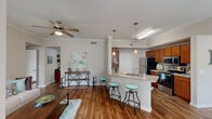 Located at 514 That Way St in Lake Jackson, TX, this well-appointed 2-bedroom, 2-bathroom residence offers a thoughtfully designed single-floor layout. The open-concept living, dining, and kitchen area serves as the heart of the home, featuring warm hardwood-style flooring, crown molding, and ceiling fans throughout. The kitchen is equipped with rich wood cabinetry, stainless steel appliances, a peninsula breakfast bar with pendant lighting, and an adjacent pantry for added storage. The dining area benefits from a large window that invites natural light, creating a bright and welcoming atmosphere. The living room continues the bright, airy feel with a generous window overlooking the outdoors. Both bedrooms are carpeted and include ceiling fans and windows with outdoor views; the primary bedroom is a comfortable, well-sized retreat with access to ample closet space, including a spacious walk-in closet with wire shelving systems. The two bathrooms feature wood vanity cabinetry and tub-shower combinations with hardwood-style flooring. A dedicated office nook with a built-in desk and floating shelves provides a functional workspace. A hallway connects all areas cohesively, completing this practical and comfortable floor plan.