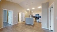Located at 19756 Pikes Peak Ave in Parker, Colorado, this single-floor residence offers a thoughtfully designed open-concept layout finished with light wood-look flooring throughout. The living area flows seamlessly into the kitchen, which is highlighted by soaring vaulted ceilings with elegant pendant lighting. The kitchen is well-appointed with white shaker-style cabinetry, a blue-gray subway tile backsplash, light countertops, and a full suite of stainless steel appliances including a refrigerator, range, and over-the-range microwave. A central island provides additional prep space and casual seating. A sliding glass door in the living area opens to a private balcony, bringing in natural light and offering pleasant views of the surrounding neighborhood. The bedrooms feature the same light flooring and neutral tones, with at least one room offering access to a spacious walk-in closet with built-in shelving. The bathrooms are finished with white cabinetry, dark countertops, large mirrors, and include a full tub-shower combination. Neutral warm and cool-toned walls throughout lend a calm, move-in-ready ambiance to the entire home.