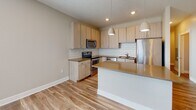 This well-designed two-story residence offers a clean, contemporary aesthetic across all living areas. The kitchen serves as a functional centerpiece, featuring light wood cabinetry, warm-toned quartz countertops, a classic white subway tile backsplash, and a full suite of stainless steel appliances including a range, microwave, dishwasher, and refrigerator. A kitchen island provides additional prep and seating space, while light hardwood-style flooring ties the area together seamlessly.

The upper level opens to a bright, airy living area with recessed lighting, warm accent walls, and a view over the staircase railing, creating an open and connected feel between floors. Bedrooms are carpeted for comfort, with natural light streaming through blinded windows and neutral wall tones throughout.

The space includes multiple bathrooms finished with wood-look tile flooring. One bathroom features a tub-shower combo with built-in shelving, while additional bathrooms offer walk-in showers with chrome fixtures and vanities with ample drawer storage.

A generously sized walk-in closet on the upper level provides extensive built-in shelving and double hanging rods, offering excellent organizational capacity. The consistent use of neutral tones, modern fixtures, and quality finishes throughout creates a cohesive and inviting living environment.